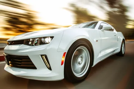 A white sports car drives at speed on a road, with the background blurred to emphasize motion.