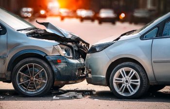Two cars involved in a front-end collision on a city street, both vehicles showing significant damage to their front ends.